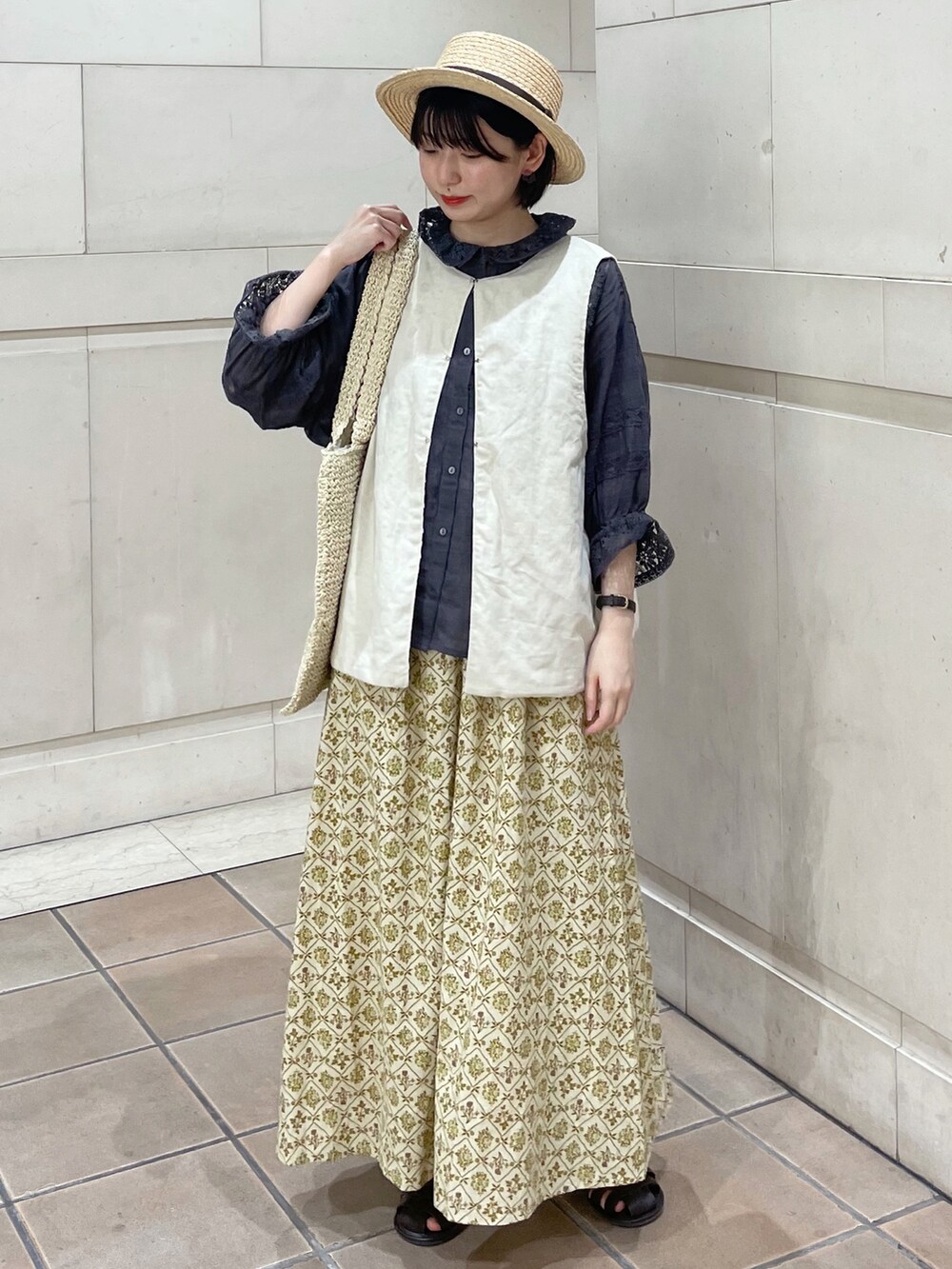 ブラウン系のサンダル、ベージュ系のスカート、ホワイト系のベストを着用したレディースの春コーディネートの2枚目の写真