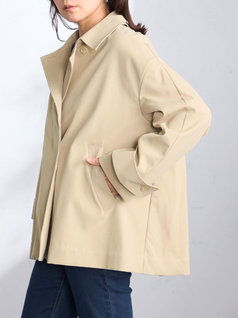 ベージュ系のステンカラーコート、ブルー系のニット/セーターを着用したレディースの春コーディネートの2枚目の写真