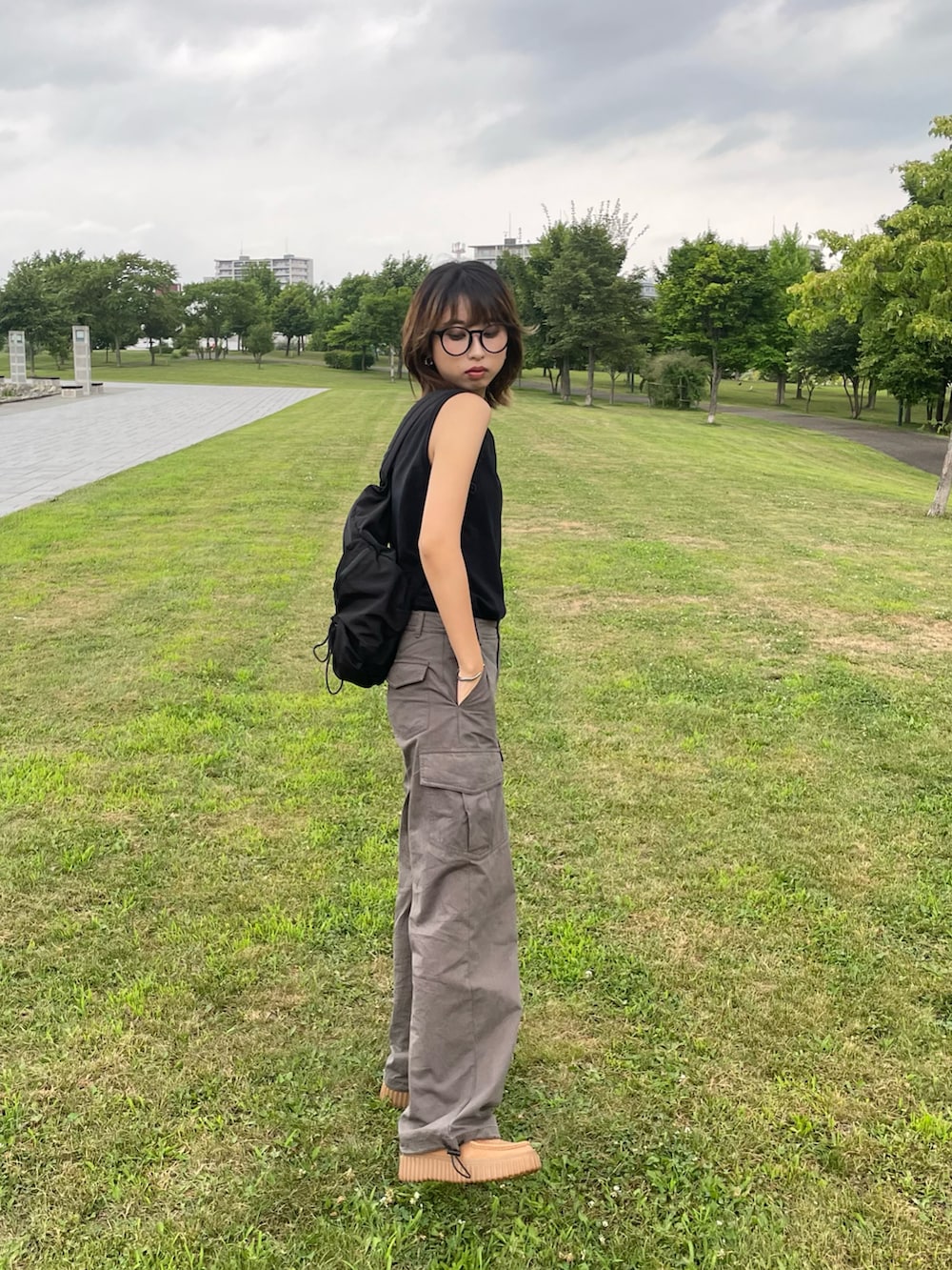 ブラック系のバックパック/リュック、グリーン系のカーゴパンツ、ブラウン系のモカシン/デッキシューズを着用したレディースの夏コーディネートの2枚目の写真