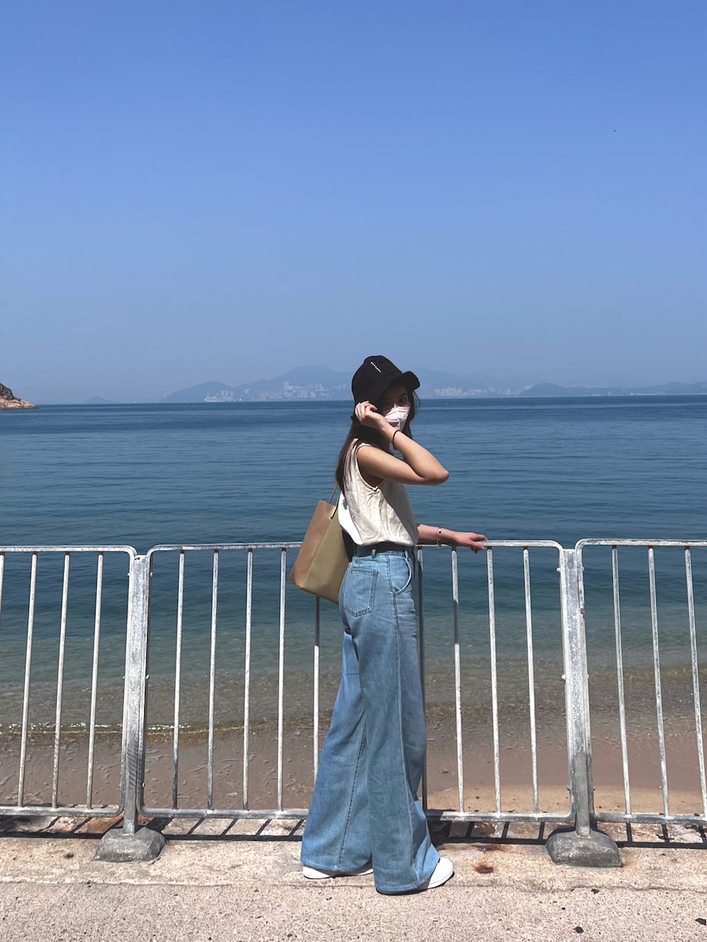 ブルー系のデニムパンツ、ベージュ系のベスト、ホワイト系のスニーカーを着用したレディースの春コーディネートの2枚目の写真