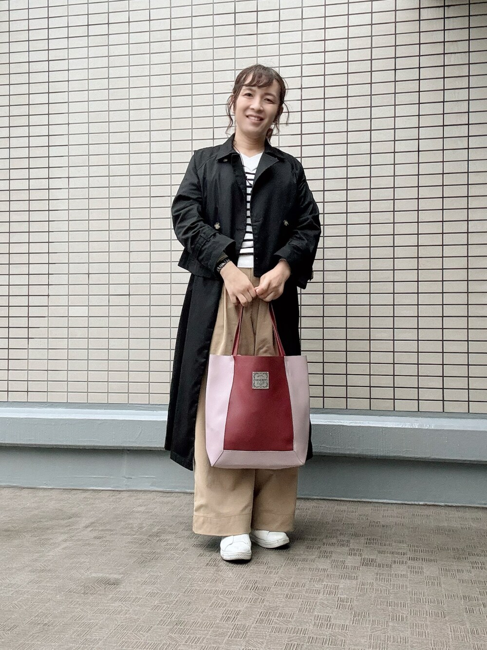 レッド系のトートバッグ、ブラック系のトレンチコート、ベージュ系のチノパンツを着用したレディースの春コーディネートの3枚目の写真
