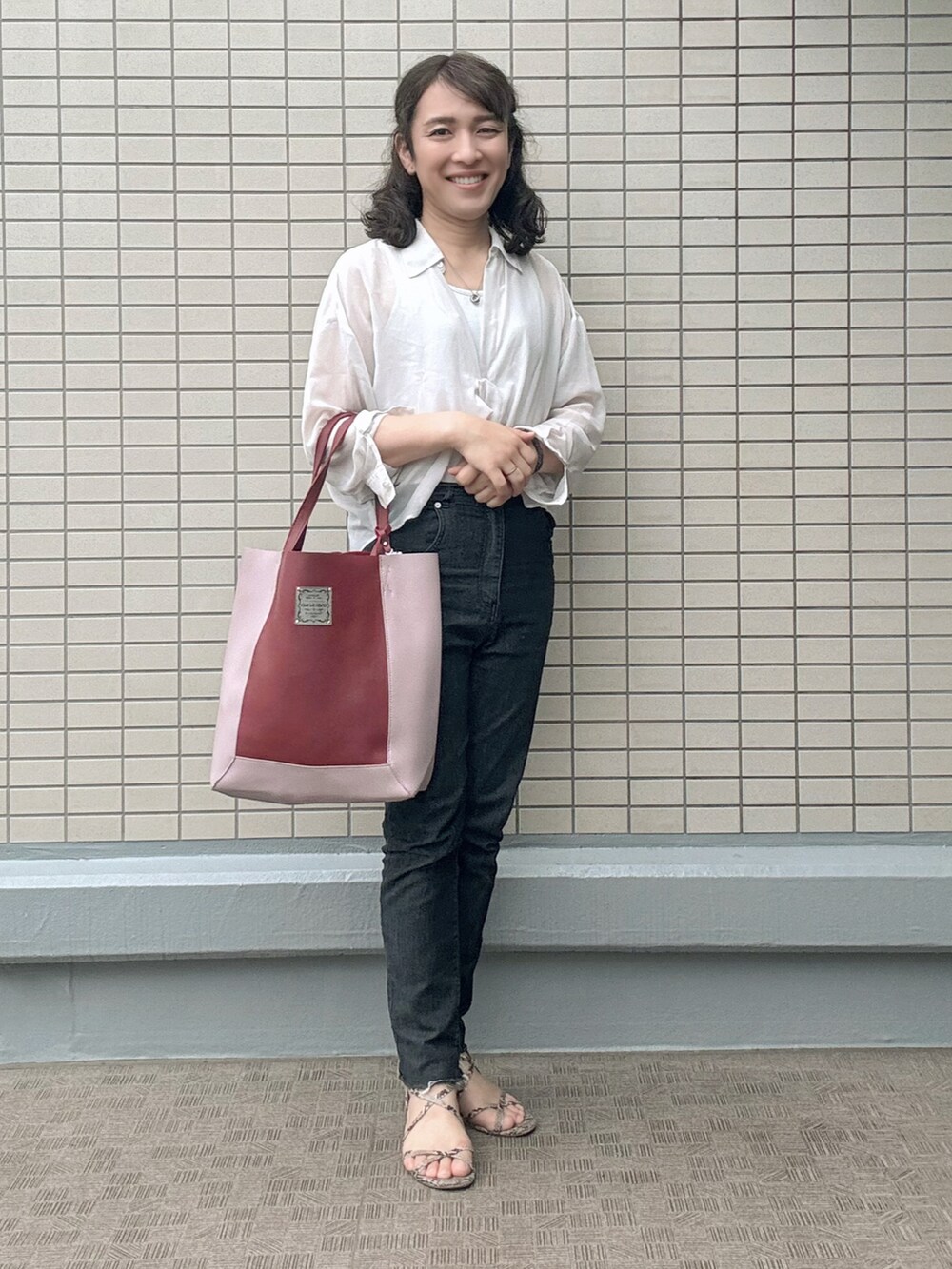 ホワイト系のトップス、ブラック系のデニムパンツ、レッド系のトートバッグを着用したレディースの春コーディネートの3枚目の写真