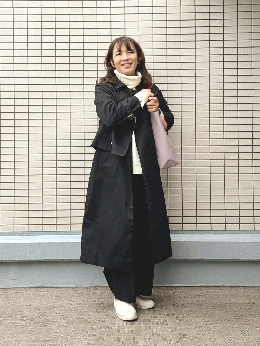 レッド系のトートバッグ、ブラック系のトレンチコート、イエロー系のニット/セーターを着用したレディースの冬コーディネートの2枚目の写真