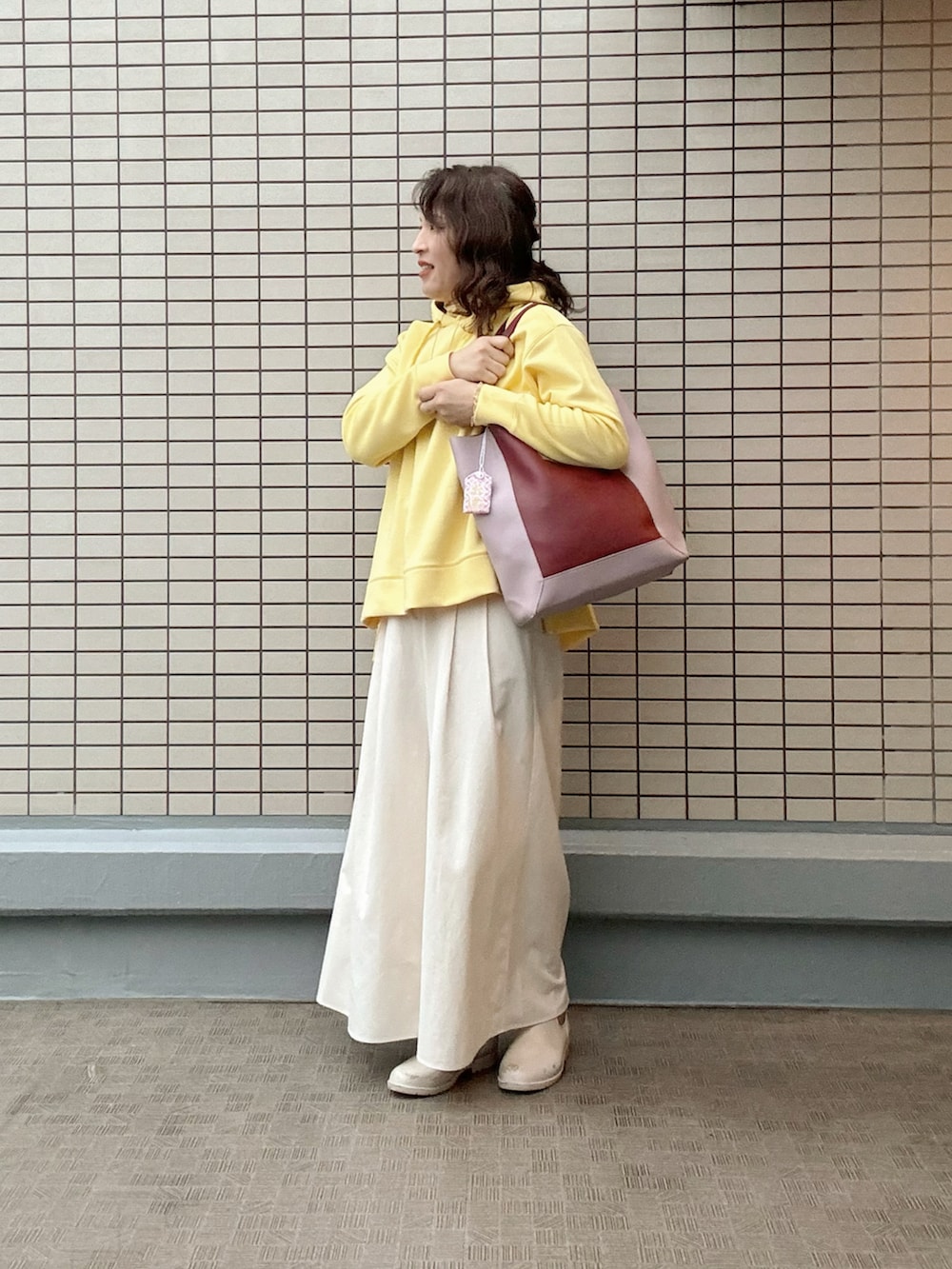 レッド系のトートバッグ、イエロー系のスウェット、ホワイト系のパンツを着用したレディースの冬コーディネートの2枚目の写真