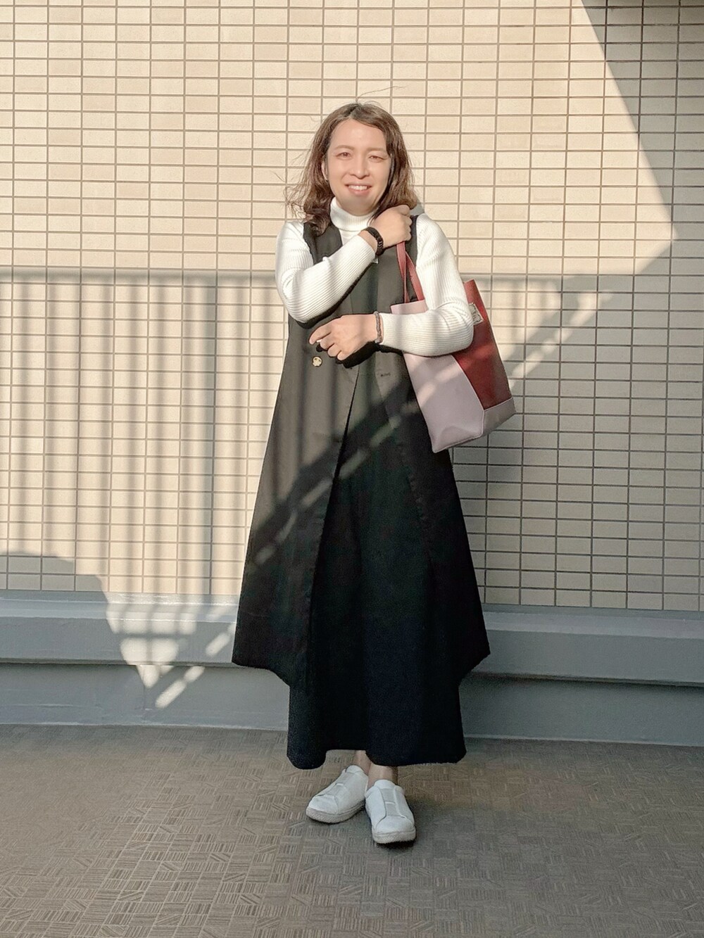 レッド系のトートバッグ、ブラック系のオールインワン・サロペット、ブラック系のトレンチコートを着用したレディースの春コーディネートの2枚目の写真