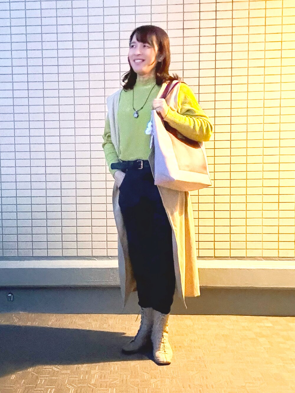 ブラック系のデニムパンツ、ベージュ系のブーツ、イエロー系のニット/セーターを着用したレディースの冬コーディネートの2枚目の写真
