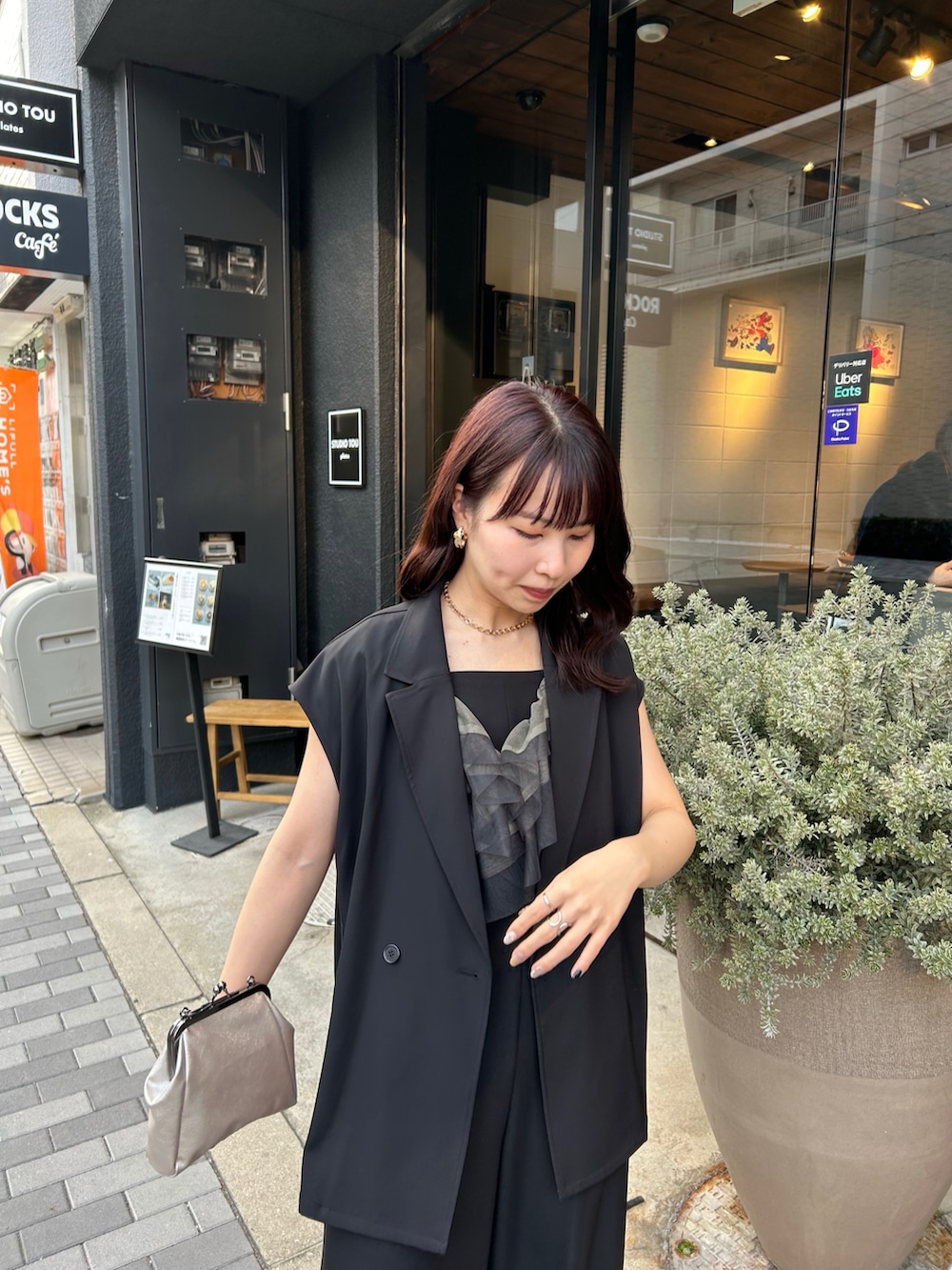 ブラック系のパンツドレス、ゴールド系のネックレス、ゴールド系のピアス（両耳用）を着用したレディースの春コーディネートの3枚目の写真