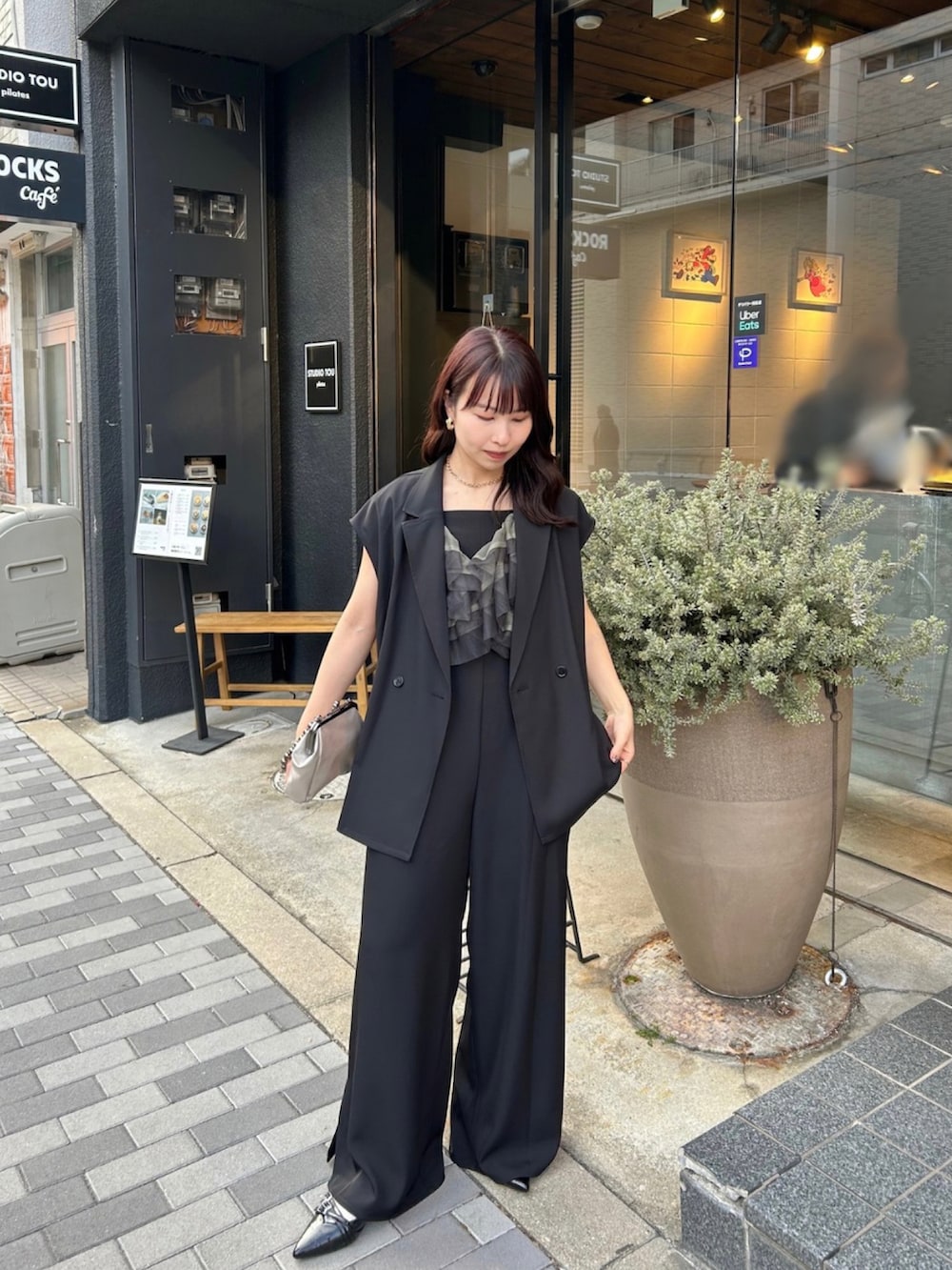 ブラック系のパンツドレス、ゴールド系のネックレス、ゴールド系のピアス（両耳用）を着用したレディースの春コーディネートの4枚目の写真