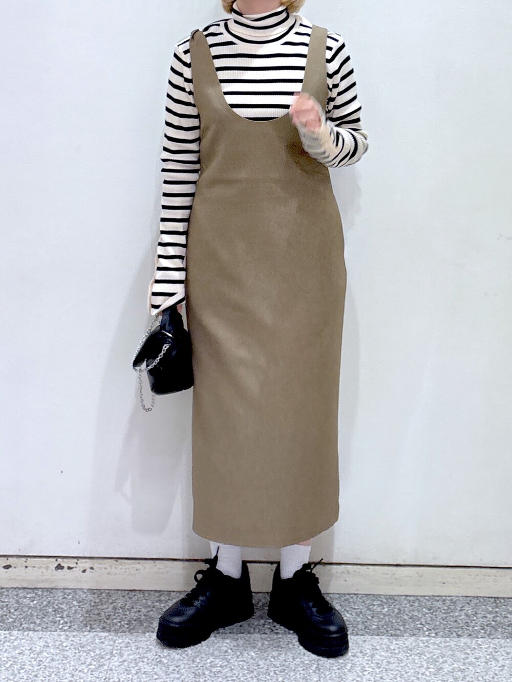 ブラック系のショルダーバッグ、ブラウン系のジャンパースカート、ベージュ系のニット/セーターを着用したレディースの冬コーディネートの5枚目の写真