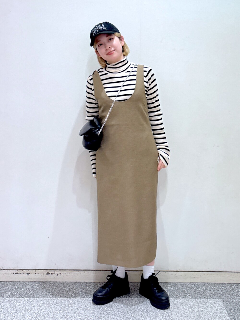 ブラック系のショルダーバッグ、ブラウン系のジャンパースカート、ベージュ系のニット/セーターを着用したレディースの冬コーディネートの2枚目の写真