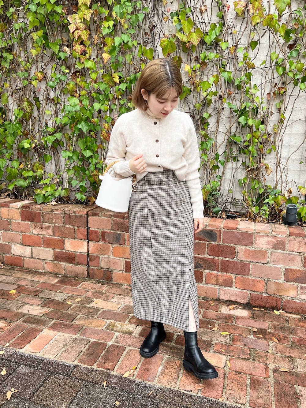 ベージュ系のスカート、ホワイト系のニット/セーター、ホワイト系のショルダーバッグを着用したレディースの冬コーディネートの2枚目の写真