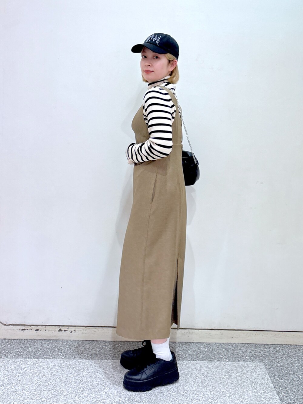 ブラック系のショルダーバッグ、ブラウン系のジャンパースカート、ベージュ系のニット/セーターを着用したレディースの冬コーディネートの3枚目の写真