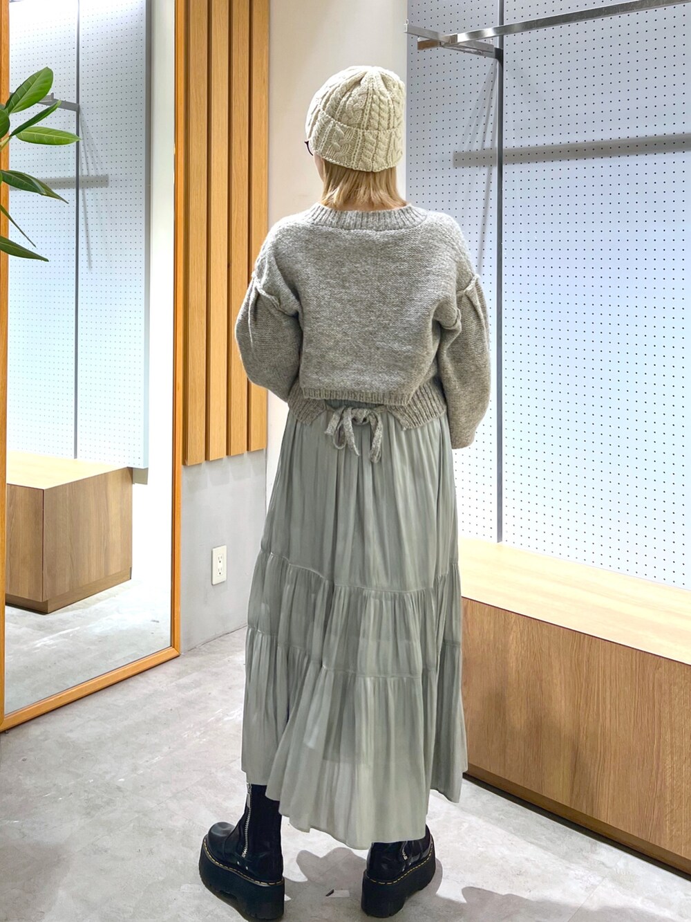 グレー系のニット/セーター、グリーン系のスカート、ホワイト系のニットキャップ/ビーニーを着用したレディースの冬コーディネートの2枚目の写真