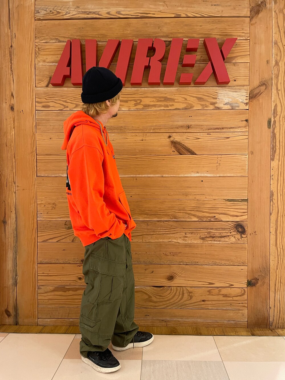 オレンジ系のパーカー、グリーン系のカーゴパンツ、ブラック系のニットキャップ/ビーニーを着用したメンズの夏コーディネートの4枚目の写真