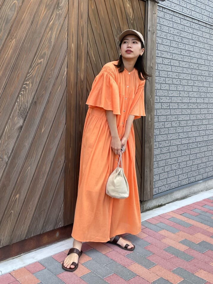 オレンジ系のワンピース、ベージュ系のハンドバッグ、ブラウン系のサンダルを着用したレディースの春コーディネートの4枚目の写真