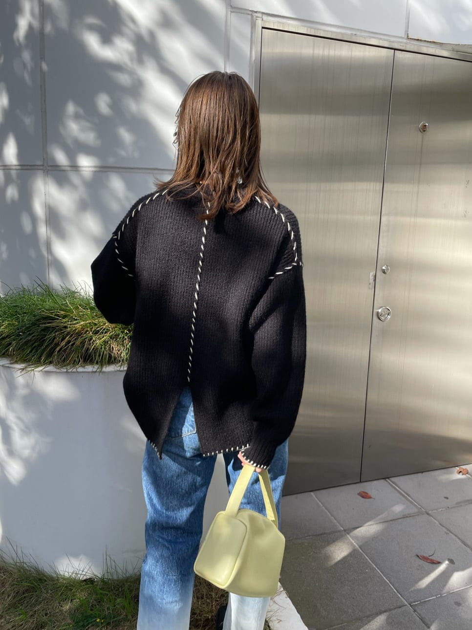 ブルー系のデニムパンツ、グリーン系のハンドバッグ、ブラック系のニット/セーターを着用したレディースの秋コーディネートの2枚目の写真