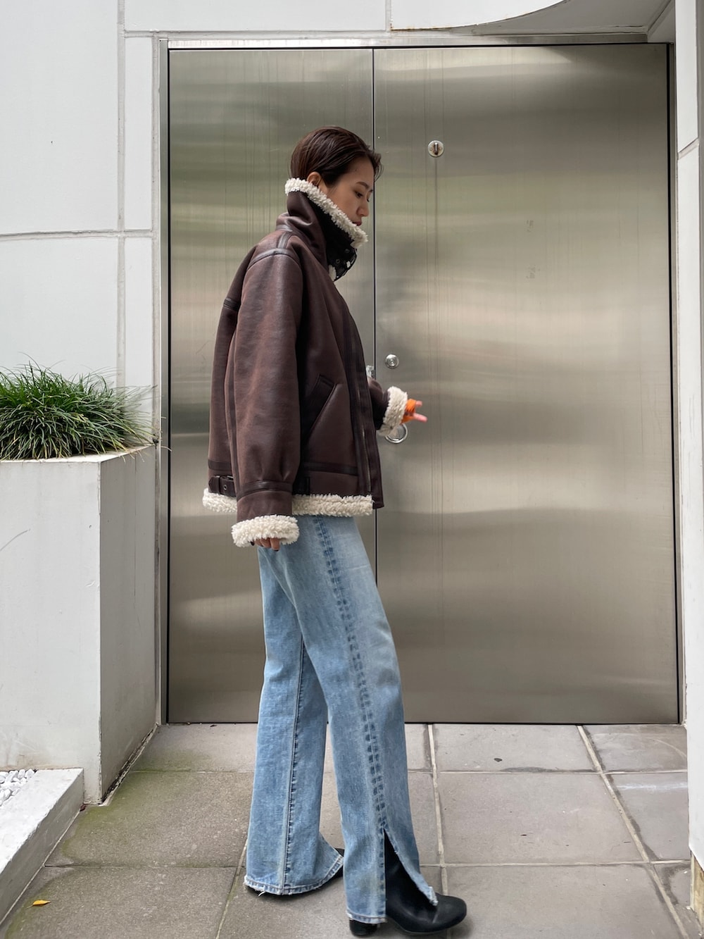 ブラウン系のムートンコート、ブルー系のデニムパンツ、ブラック系のブーツを着用したレディースの秋コーディネートの4枚目の写真