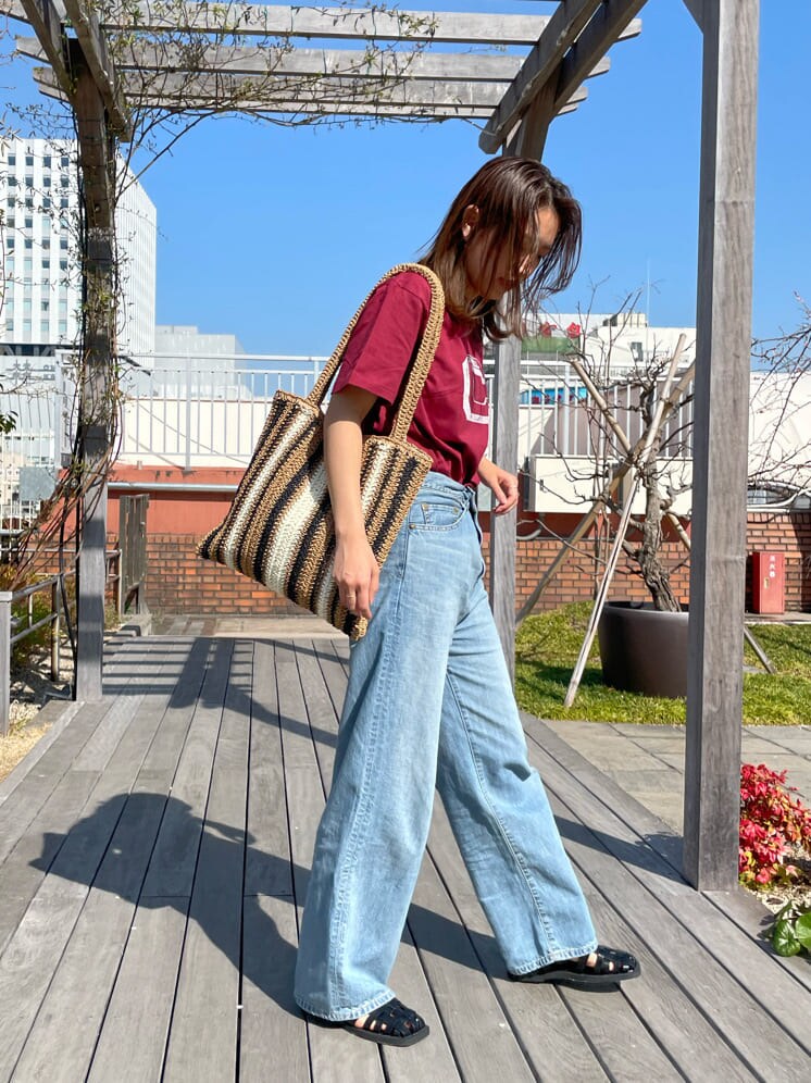ベージュ系のトートバッグ、ブラック系のサンダル、ブルー系のデニムパンツを着用したレディースの春コーディネートの4枚目の写真