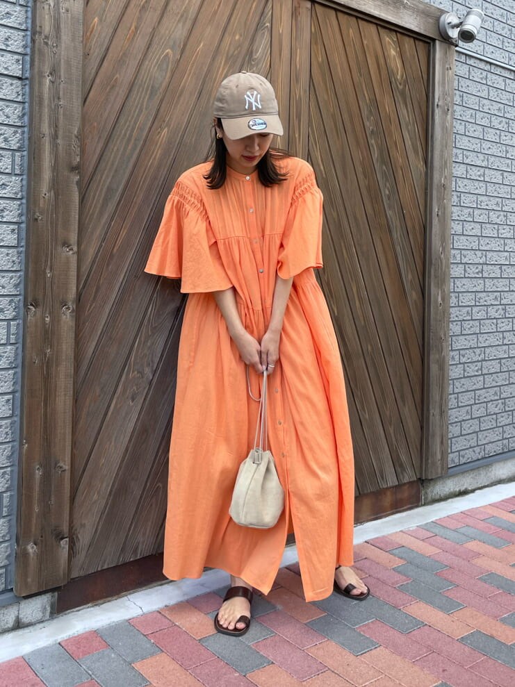 オレンジ系のワンピース、ベージュ系のハンドバッグ、ブラウン系のサンダルを着用したレディースの春コーディネートの5枚目の写真