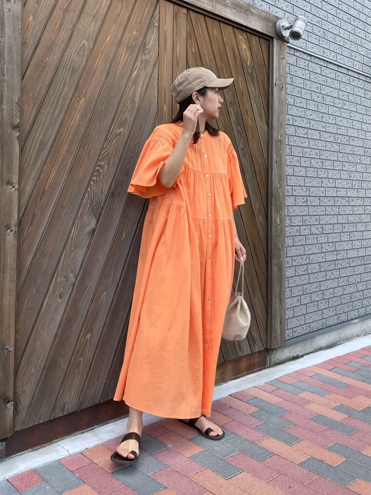 オレンジ系のワンピース、ベージュ系のハンドバッグ、ブラウン系のサンダルを着用したレディースの春コーディネートの3枚目の写真
