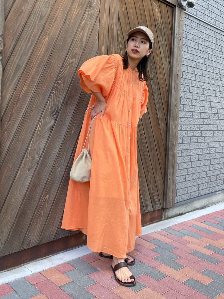 オレンジ系のワンピース、ベージュ系のハンドバッグ、ブラウン系のサンダルを着用したレディースの春コーディネートの2枚目の写真