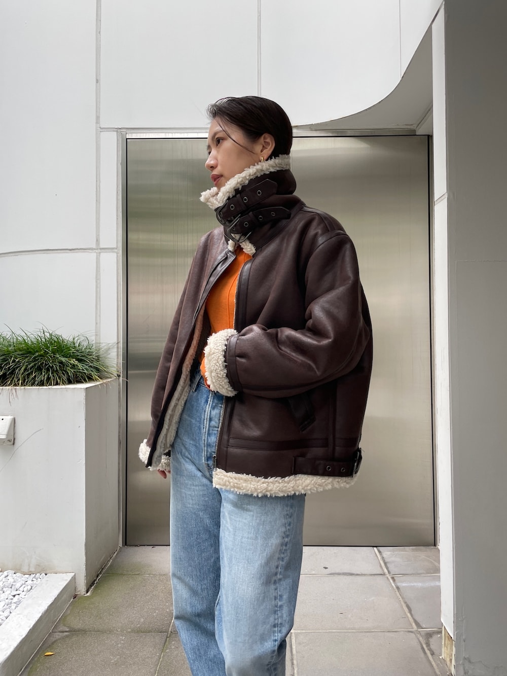 ブラウン系のムートンコート、ブルー系のデニムパンツ、ブラック系のブーツを着用したレディースの秋コーディネートの6枚目の写真