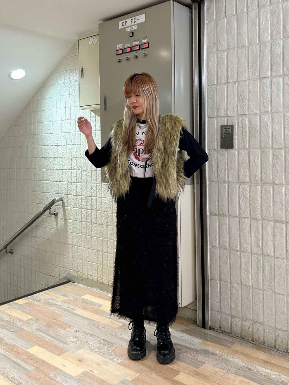 ブラック系のスカート、ブラック系のブーツ、ベージュ系のベストを着用したレディースの秋コーディネートの2枚目の写真