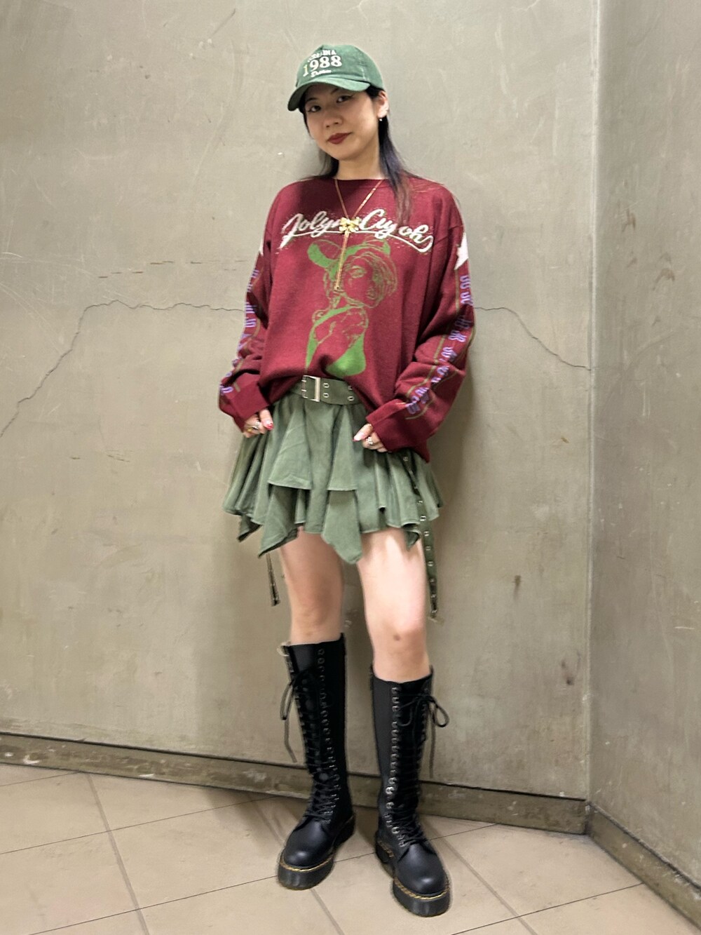 ブラック系のブーツ、レッド系のニット/セーター、グリーン系のスカートを着用したレディースの秋コーディネートの2枚目の写真