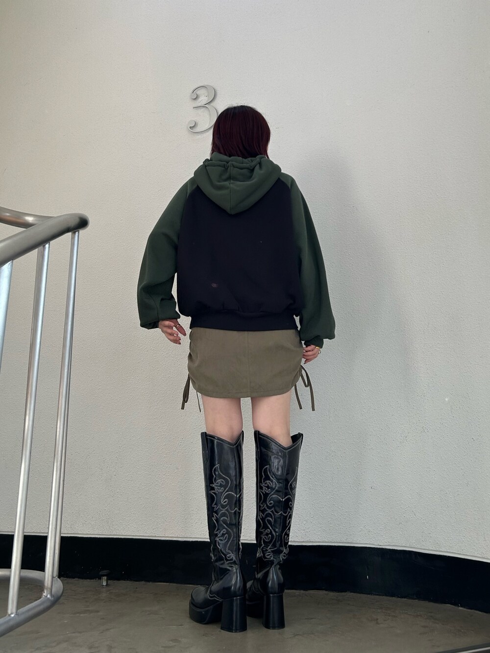 ブラック系のブーツ、グリーン系のスカート、ブラック系のパーカーを着用したレディースの冬コーディネートの2枚目の写真