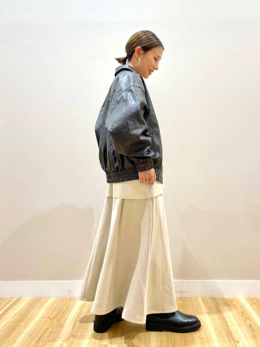 ブラック系のブーツ、ベージュ系のショルダーバッグ、ベージュ系のスカートを着用したレディースの秋コーディネートの2枚目の写真