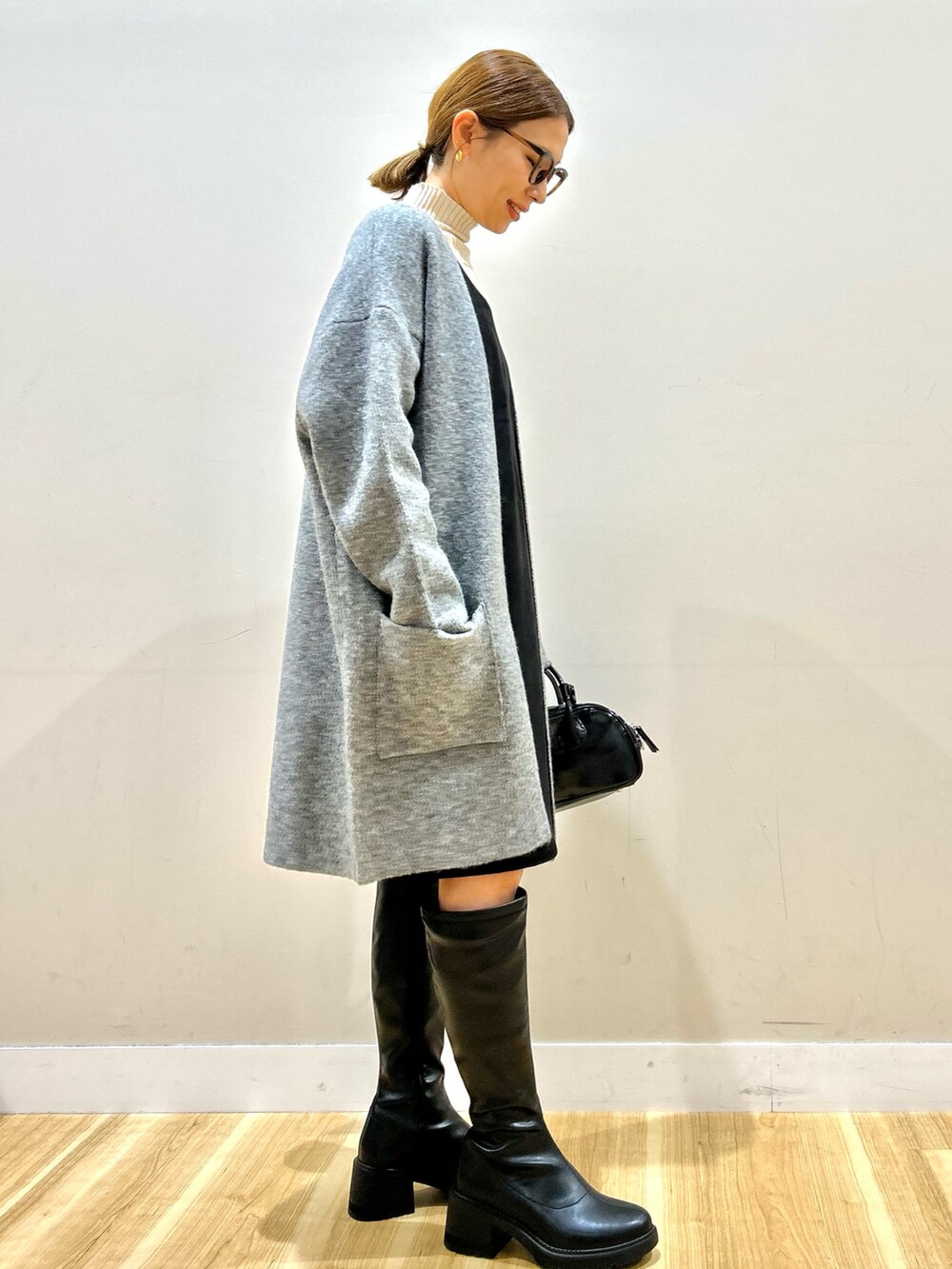 グレー系のノーカラーコート、ブラック系のワンピース、ホワイト系のニット/セーターを着用したレディースの秋コーディネートの2枚目の写真