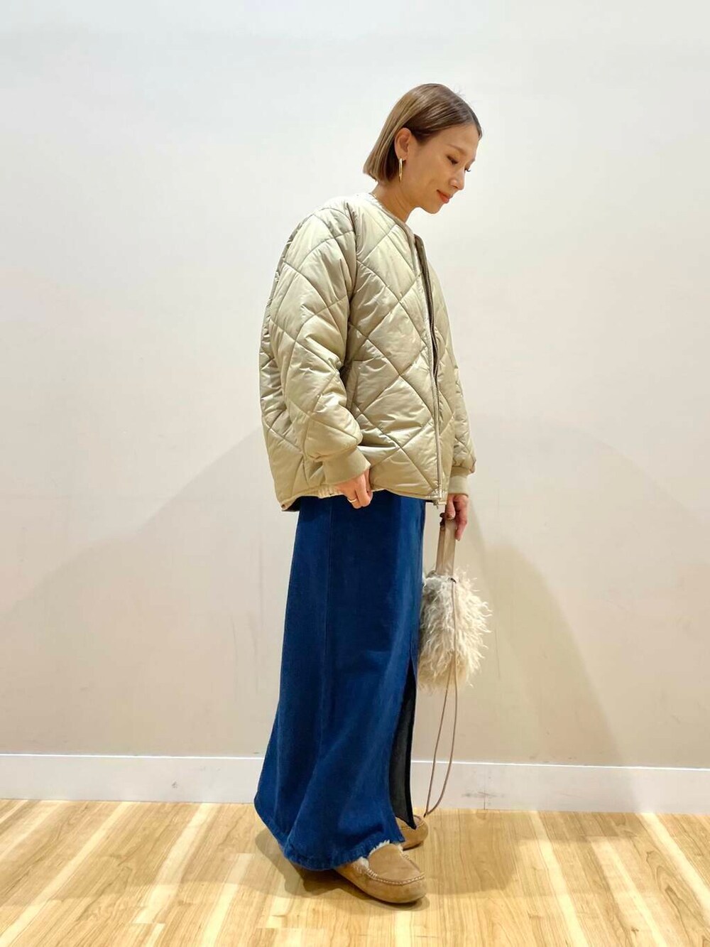 ベージュ系のショルダーバッグ、ブルー系のスカート、ベージュ系のダウンジャケット/コートを着用したレディースの秋コーディネートの3枚目の写真