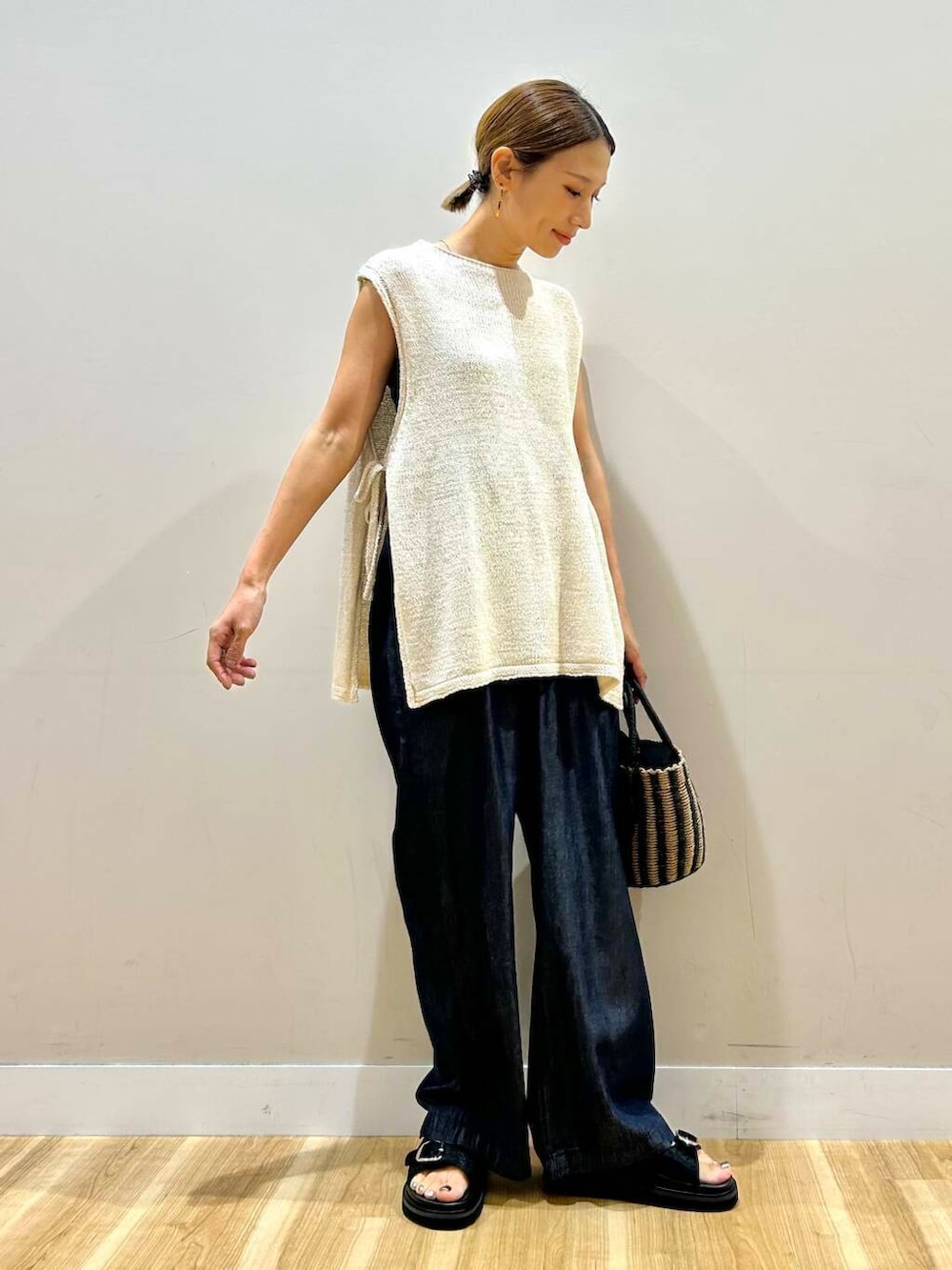 ブラック系のハンドバッグ、ブルー系のデニムパンツ、ホワイト系のベストを着用したレディースの夏コーディネートの3枚目の写真