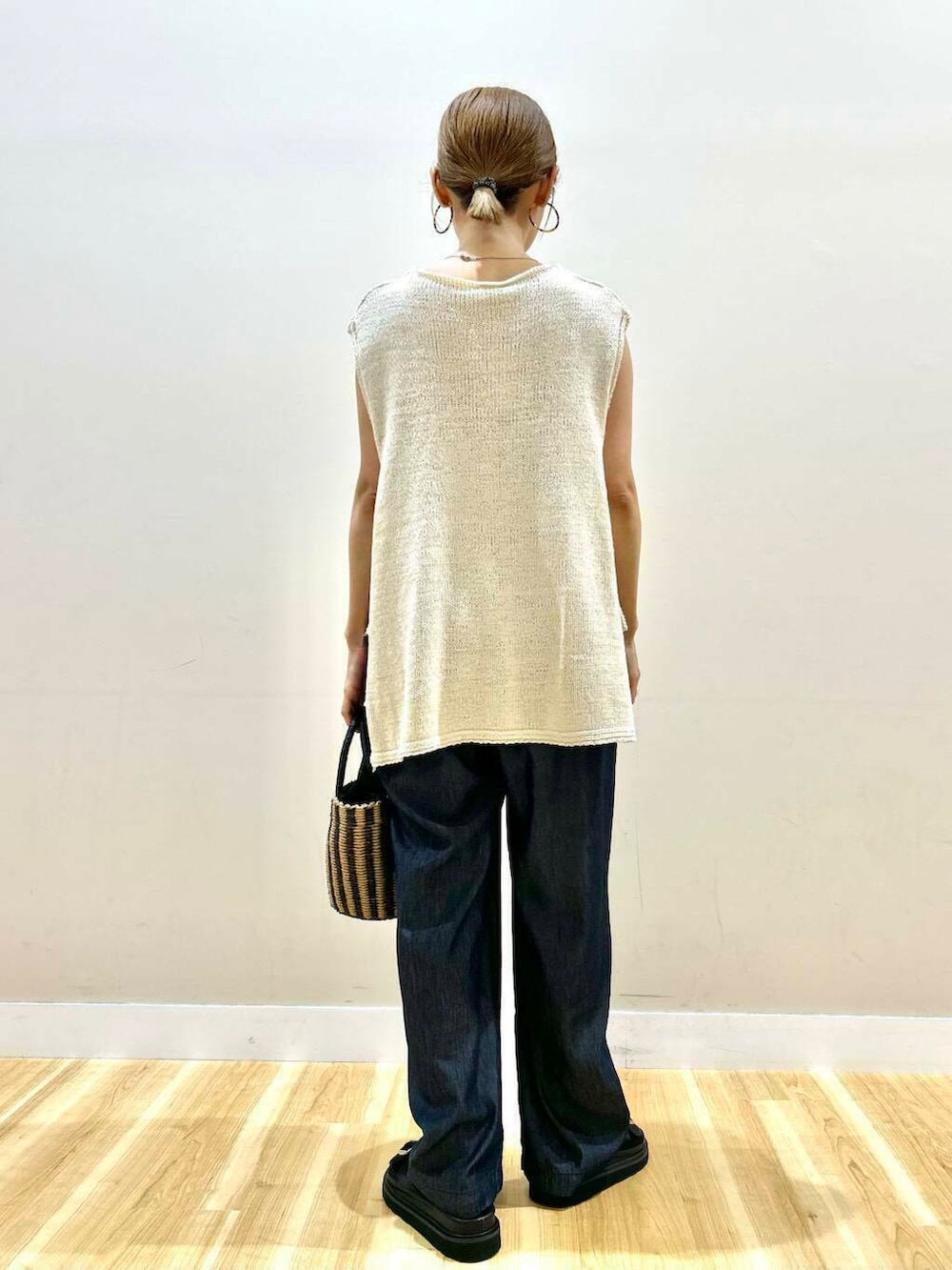 ブラック系のハンドバッグ、ブルー系のデニムパンツ、ホワイト系のベストを着用したレディースの夏コーディネートの5枚目の写真