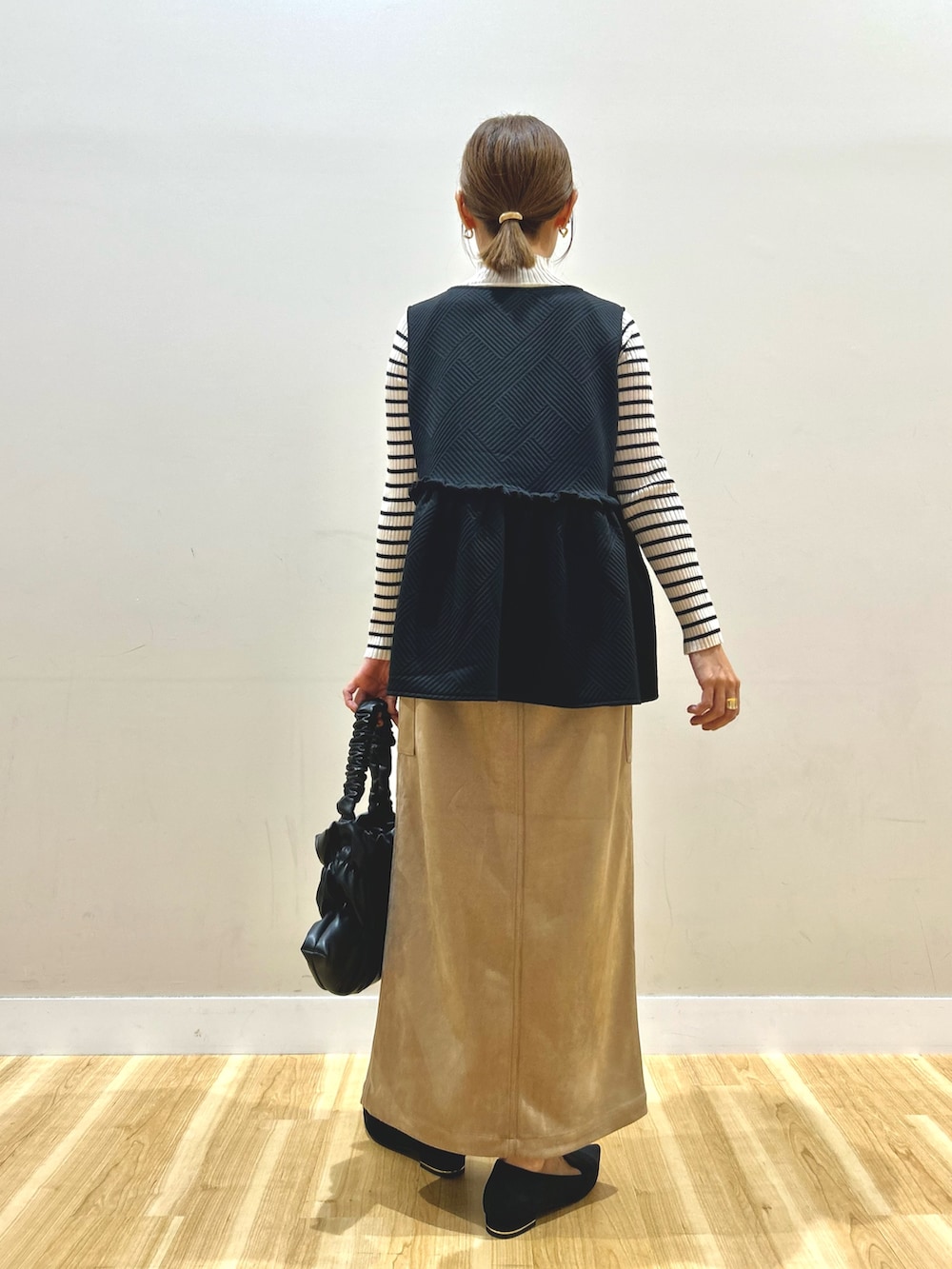 ブラック系のベスト、ホワイト系のニット/セーター、ブラウン系のスカートを着用したレディースの秋コーディネートの3枚目の写真