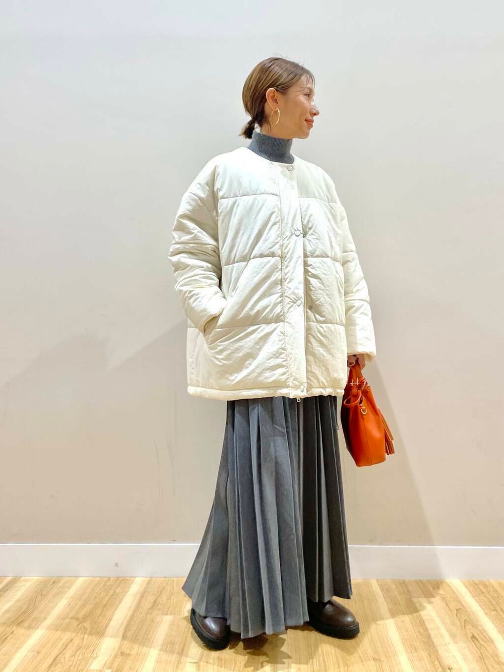 ブラウン系のブーツ、オレンジ系のショルダーバッグ、グレー系のスカートを着用したレディースの冬コーディネートの3枚目の写真