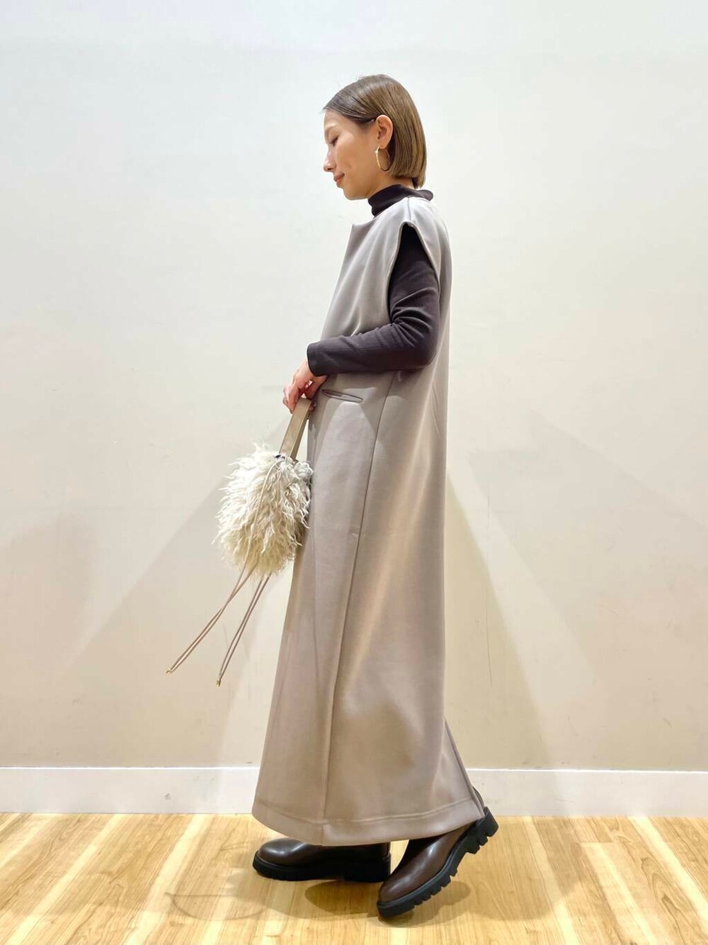 ブラウン系のブーツ、ベージュ系のショルダーバッグ、ブラウン系のジャンパースカートを着用したレディースの秋コーディネートの2枚目の写真