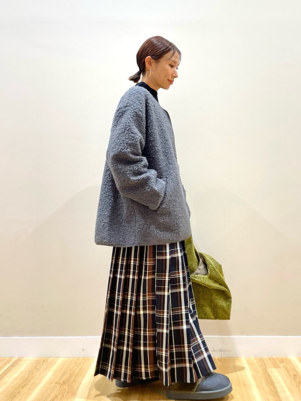 グレー系のノーカラーコート、ブラック系のニット/セーター、ブルー系のスカートを着用したレディースの冬コーディネートの2枚目の写真