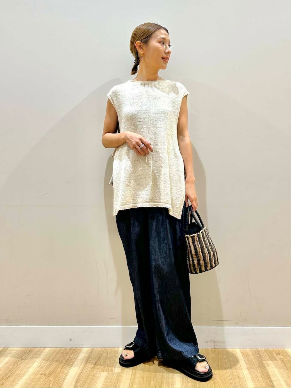 ブラック系のハンドバッグ、ブルー系のデニムパンツ、ホワイト系のベストを着用したレディースの夏コーディネートの2枚目の写真