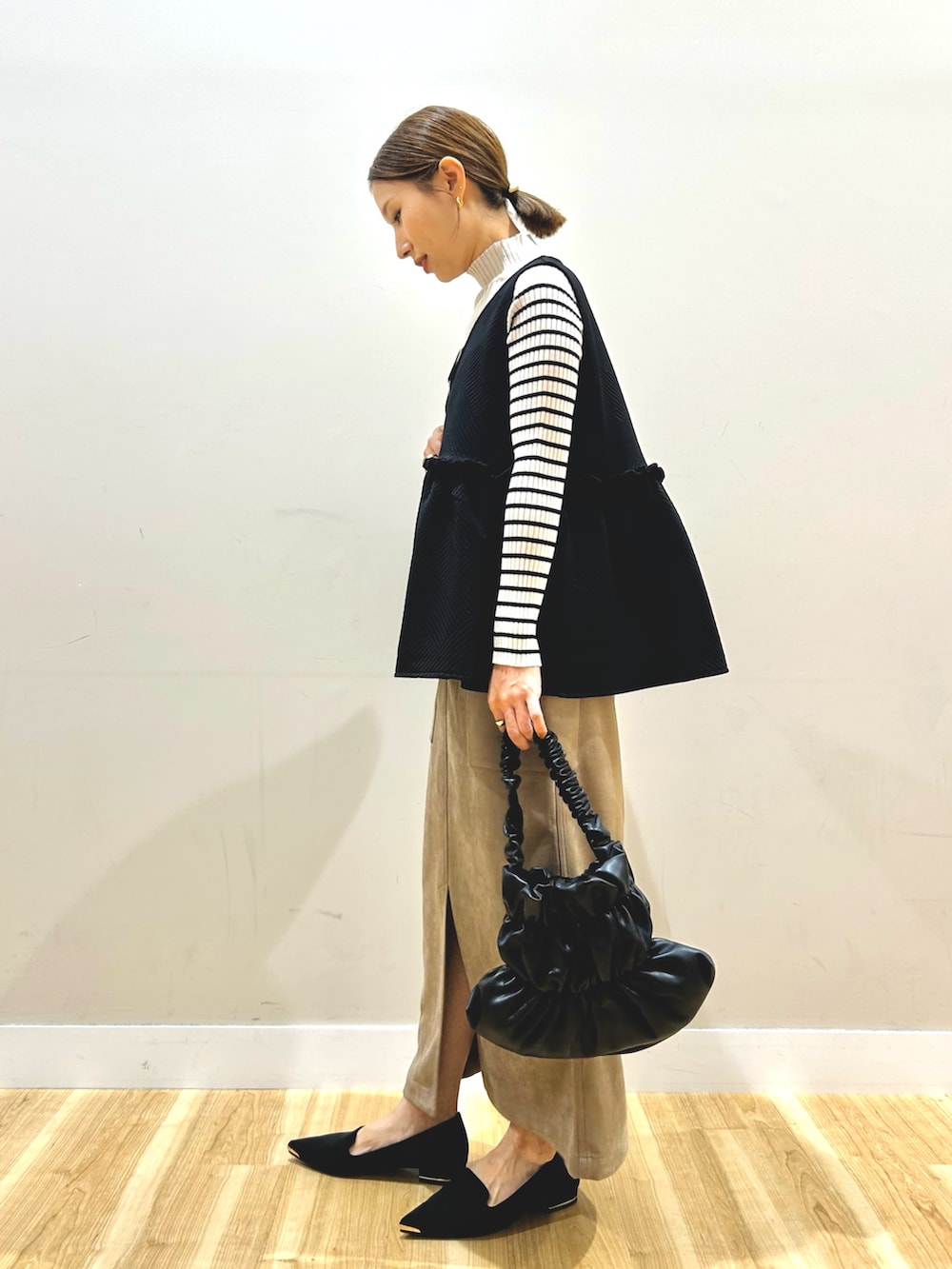 ブラック系のベスト、ホワイト系のニット/セーター、ブラウン系のスカートを着用したレディースの秋コーディネートの2枚目の写真