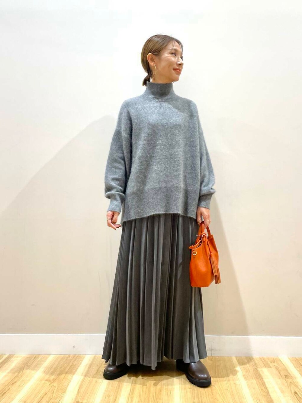 ブラウン系のブーツ、オレンジ系のショルダーバッグ、グレー系のスカートを着用したレディースの冬コーディネートの2枚目の写真