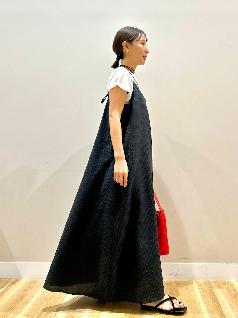 レッド系のショルダーバッグ、ブラック系のサンダル、ブラック系のワンピースを着用したレディースの夏コーディネートの2枚目の写真