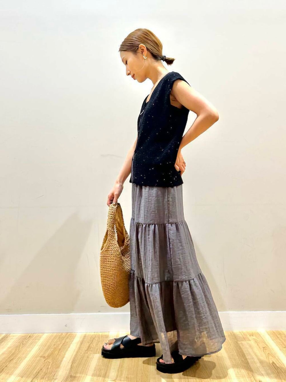 イエロー系のトートバッグ、ブラック系のサンダル、ブラック系のベストを着用したレディースの夏コーディネートの2枚目の写真