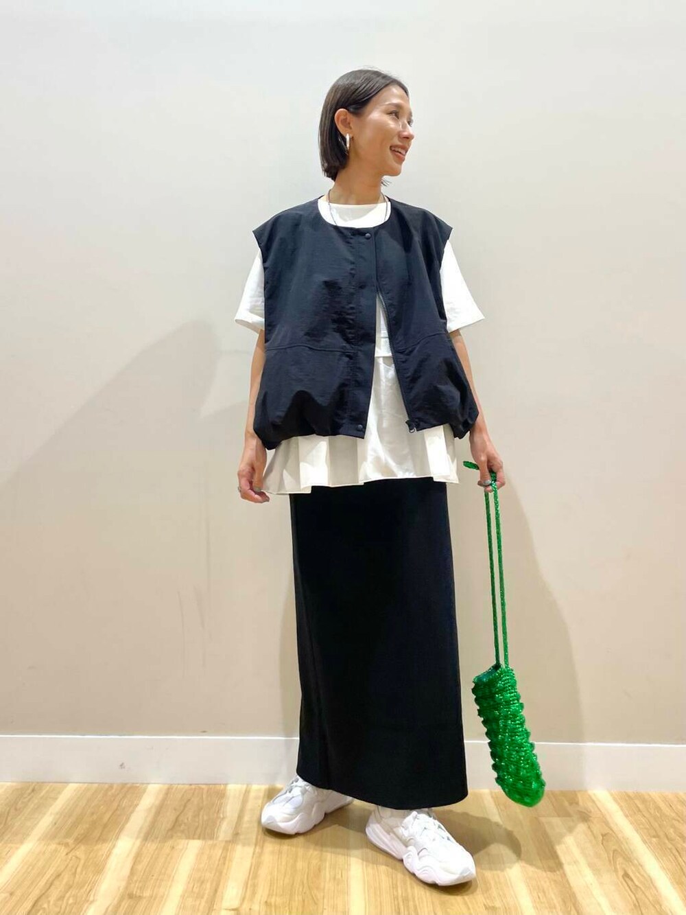 ホワイト系のスニーカー、グリーン系のショルダーバッグ、ブラック系のスカートを着用したレディースの秋コーディネートの2枚目の写真