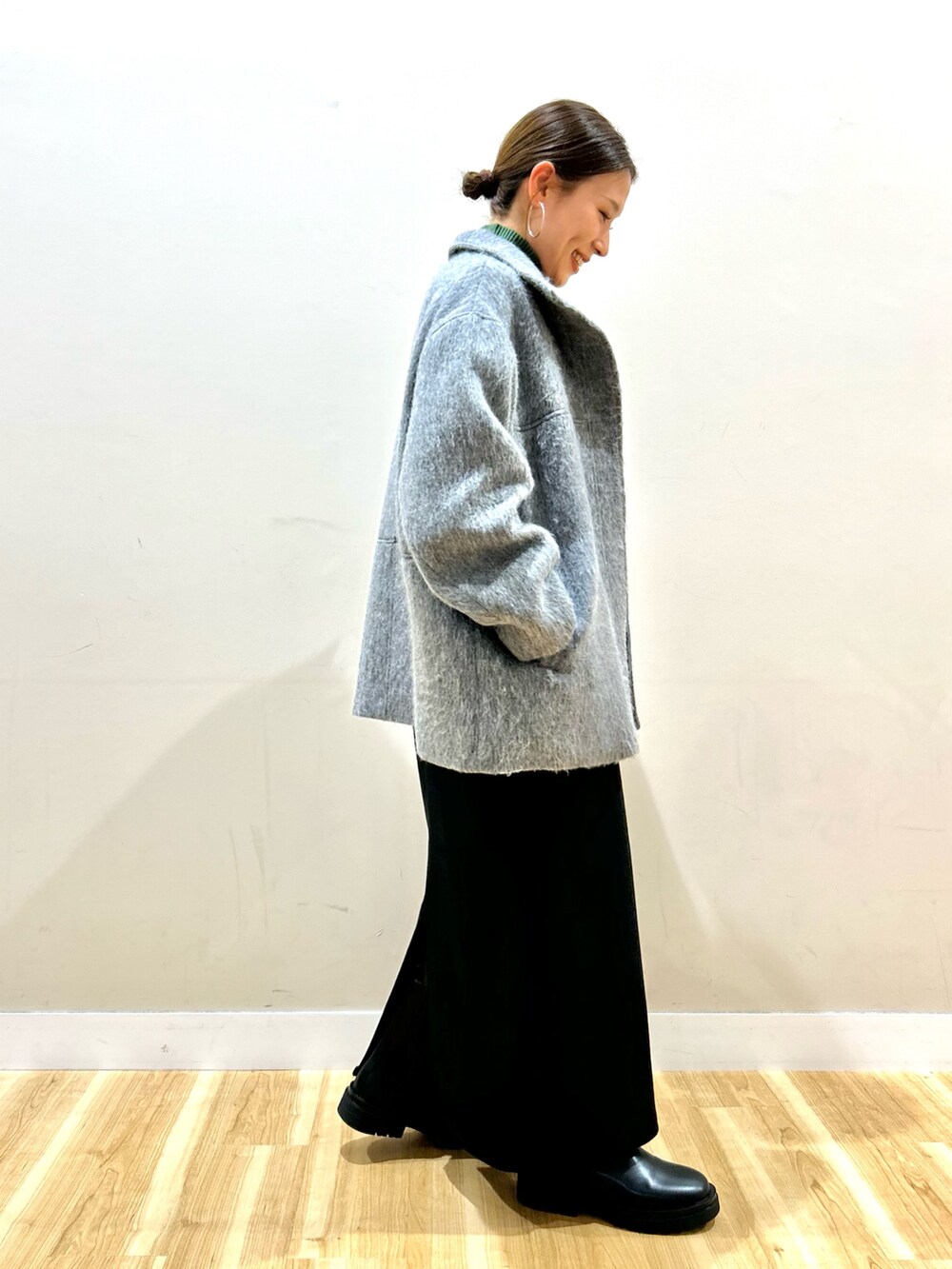 グレー系のその他アウター、グリーン系のニット/セーター、ブラック系のジャンパースカートを着用したレディースの冬コーディネートの3枚目の写真