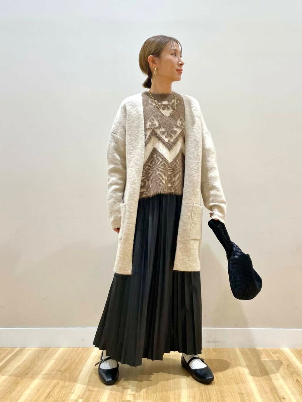 ブラック系のパンプス、ブラック系のハンドバッグ、ベージュ系のカーディガン/ボレロを着用したレディースの冬コーディネートの2枚目の写真
