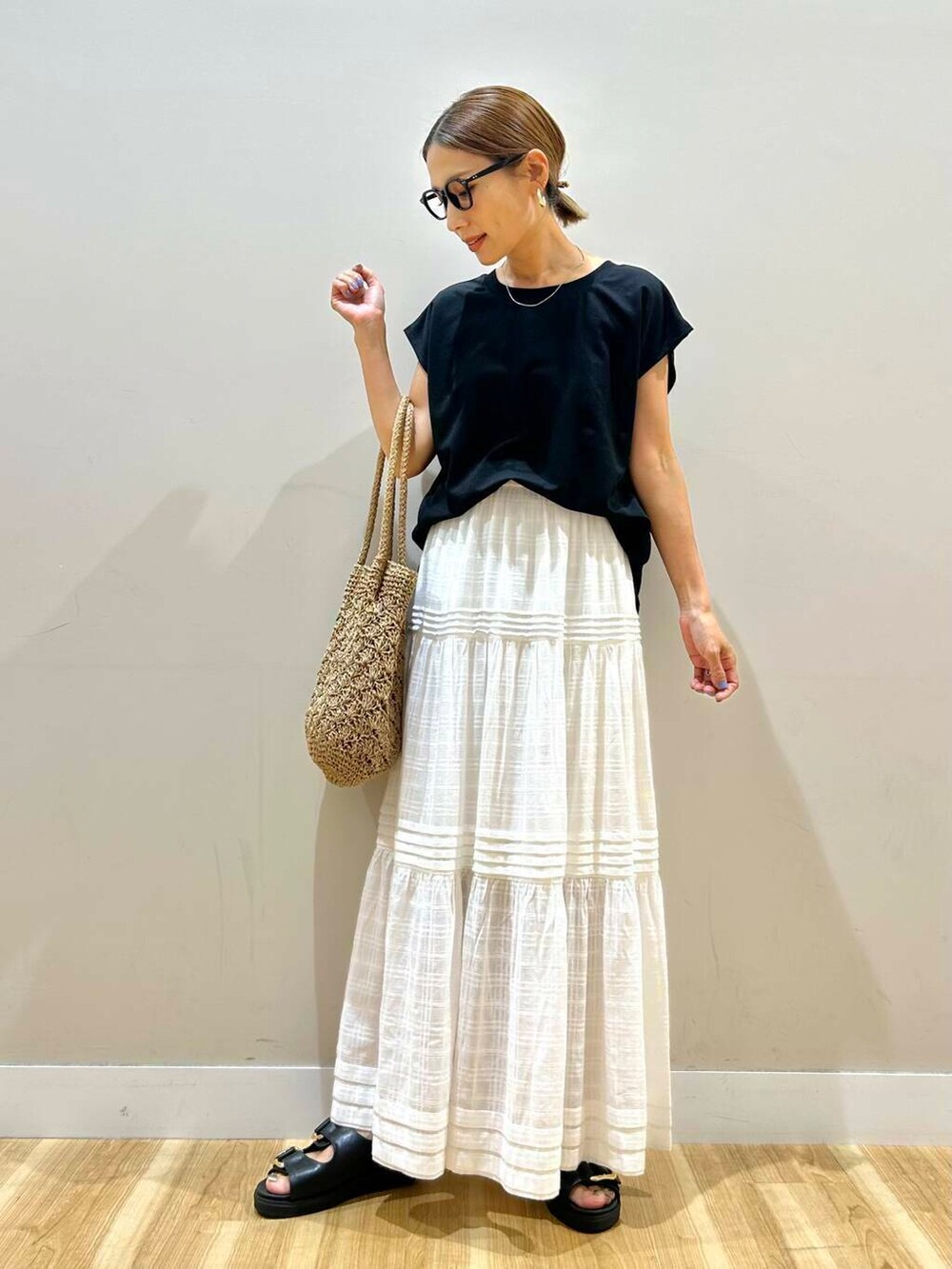 ブラック系のサンダル、ベージュ系のトートバッグ、ホワイト系のスカートを着用したレディースの夏コーディネートの2枚目の写真