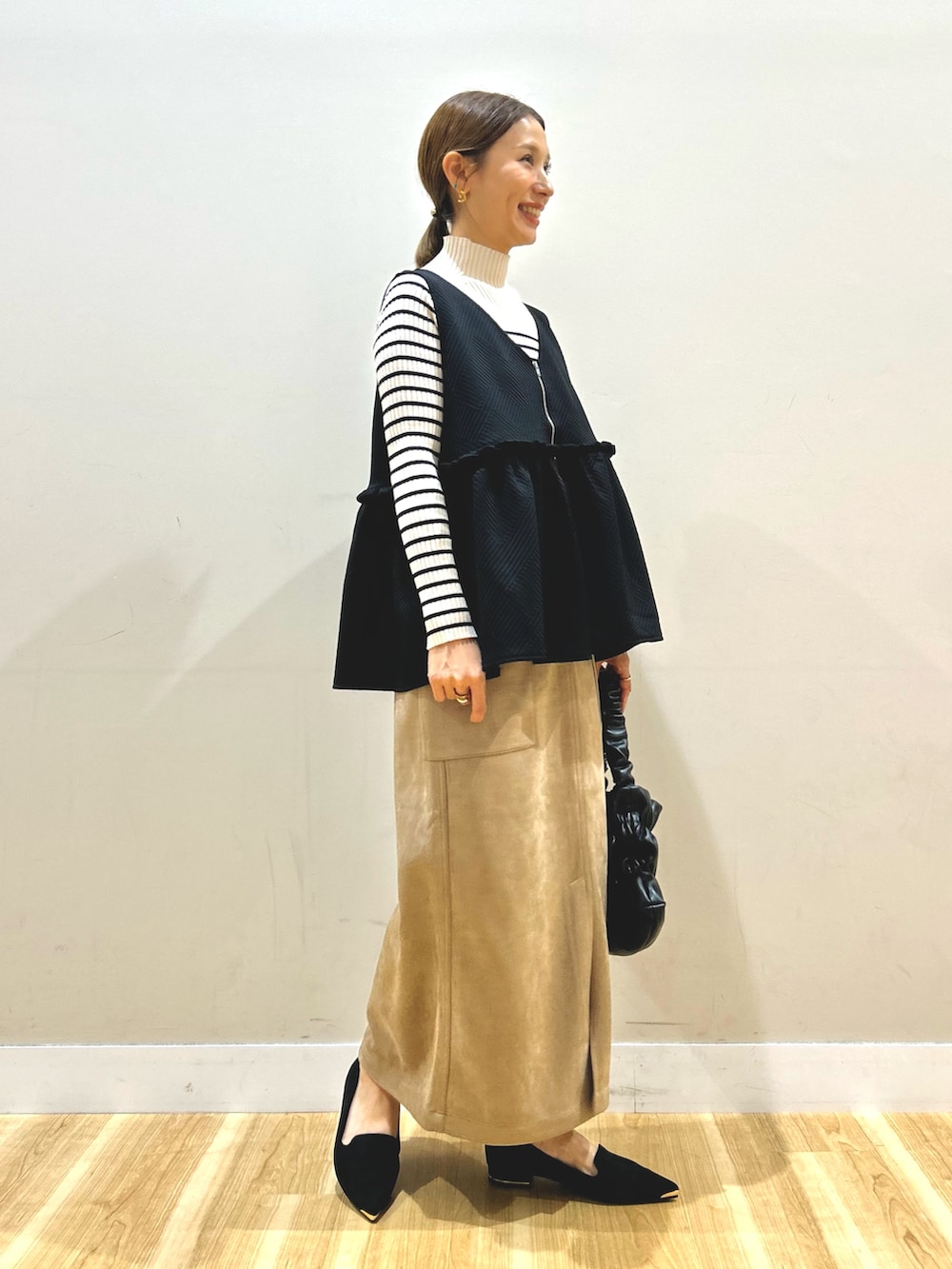 ブラック系のベスト、ホワイト系のニット/セーター、ブラウン系のスカートを着用したレディースの秋コーディネートの6枚目の写真