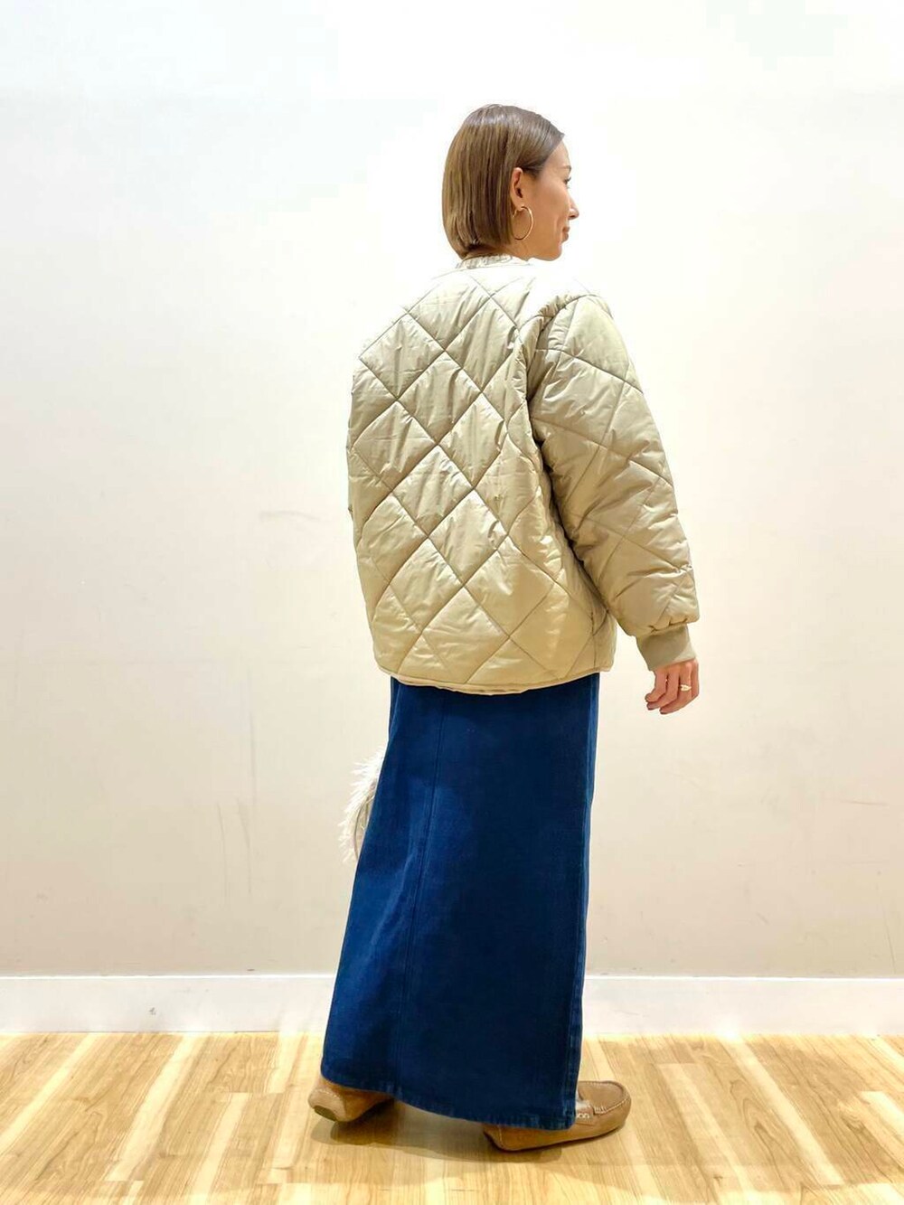 ベージュ系のショルダーバッグ、ブルー系のスカート、ベージュ系のダウンジャケット/コートを着用したレディースの秋コーディネートの4枚目の写真