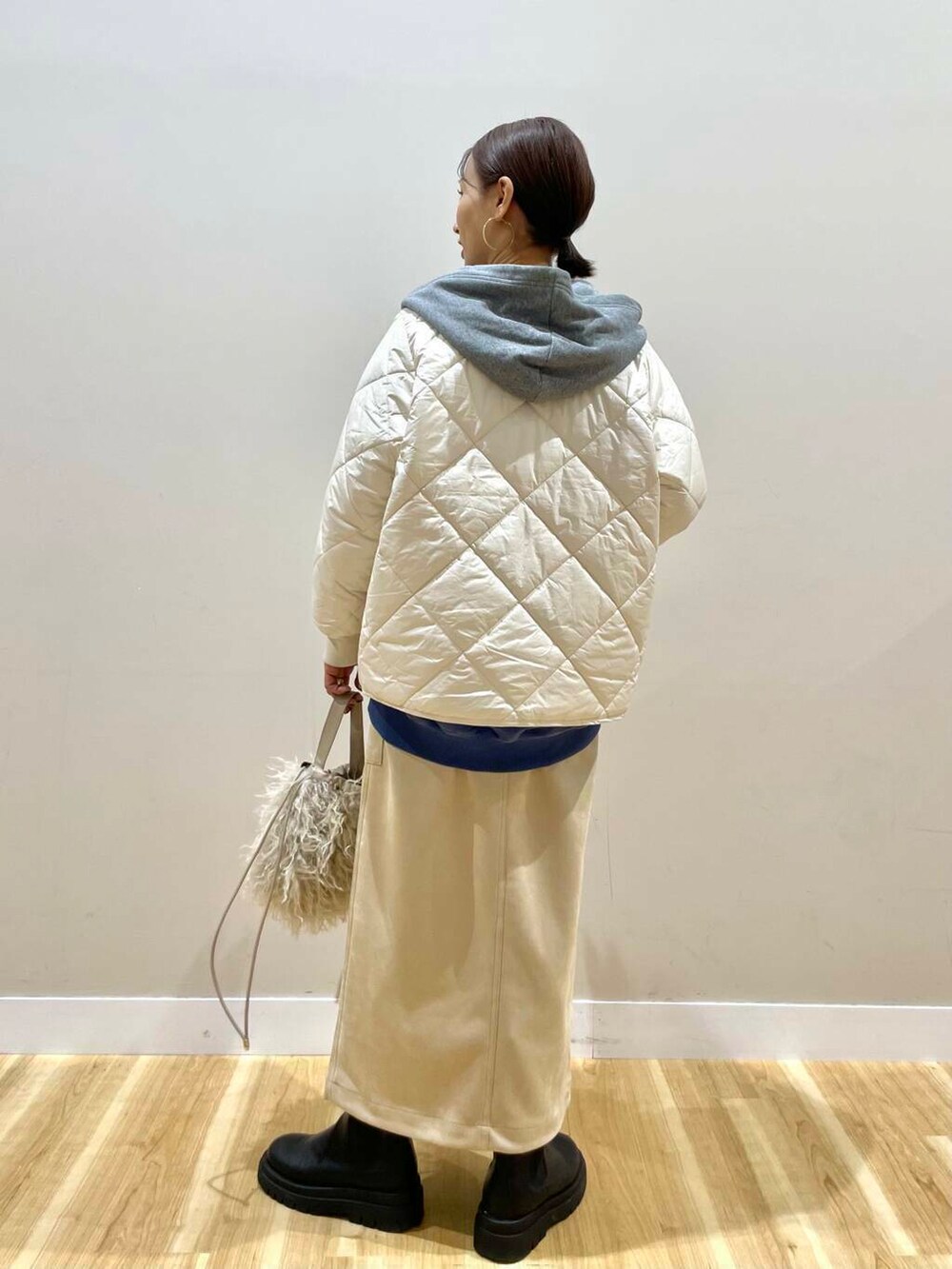ベージュ系のショルダーバッグ、ホワイト系のスカート、グレー系のパーカーを着用したレディースの冬コーディネートの3枚目の写真